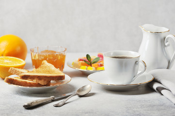 Coffee and toast with orange jam.  The concept of an elegant breakfast setting.  Oranges, cream, marmalade complete the composition.  Light background.  Close-up.