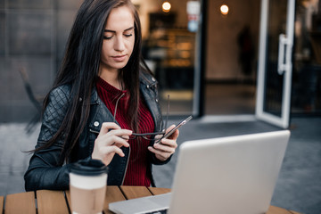 Young pretty woman  with smartphone and cup of coffee sit on city street