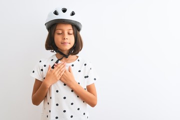 Beautiful child girl wearing security bike helmet standing over isolated white background smiling with hands on chest with closed eyes and grateful gesture on face. Health concept.