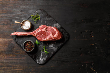 Raw Tomahawk steak on wooden background with spices for grilling, top view, copy space