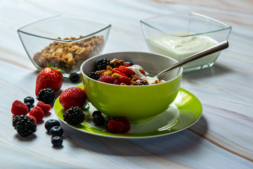 A bowl of cereal, soft fruit and yogurt. Table top on white marble. With strawberries, blueberries, raspberries and blackberries.