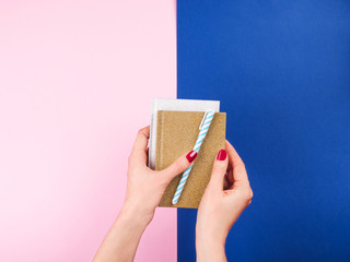Duotone pink and classic blue background with glitter notebooks and pen in female hands with red...