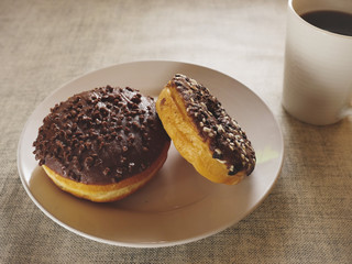 Two chocolate doughnut on a white plate and a cup of tea on a simple table cloth, Concept break, breakfast.