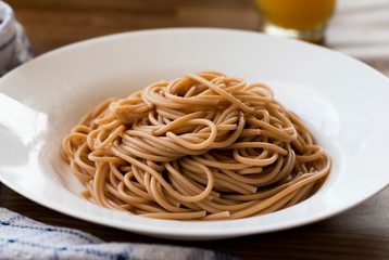 Cooked whole wheat pasta without sauce on wooden table in white plate. Spaghetti with healthy quinoa pasta.
