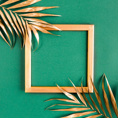 Gold tropical palm leaves and photo frame on green background. Flat lay, top view minimal concept.
