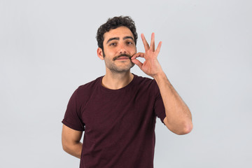 Brown, smiling, handsome man touching his mustache with purple t-shirt. Funny portrait. Gray...