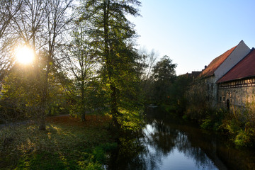 Fototapeta na wymiar A stream with nature and old houses in the evening light with sun