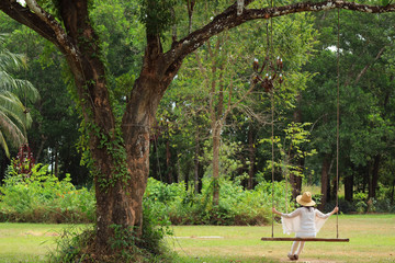 Woman relaxing on wooden swing under the big tree in the park