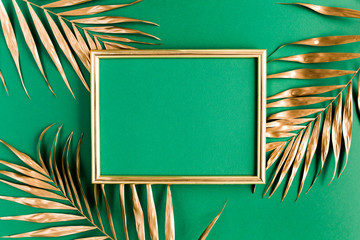 Gold tropical palm leaves and photo frame on green background. Flat lay, top view minimal concept.