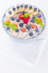 Healthy breakfast. Oatmeal with blueberries, banana and raspberry. Oatmeal with fruits and nuts in a bowl. Cooked oatmeal on white background. Vegetarian food. Copy space