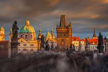 Naklejka premium Prague, Czech Republic - Massive crowd on the world famous Charles Bridge (Karluv most) with St. Francis of Assisi Church and beautiful golden sky and moving clouds on a winter afternoon