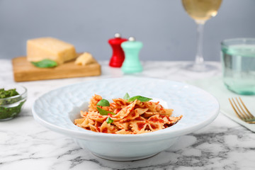 Tasty pasta with tomato sauce and basil on white marble table