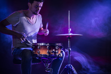 Fototapeta na wymiar A drummer plays drums on a blue background. Beautiful special effects of light and smoke. The process of playing a musical instrument.