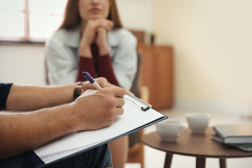 Professional psychotherapist and patient in office, focus on hands with clipboard