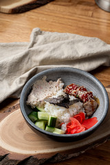 Eel poke bowl with rice, ginger and cucumber on wooden table with knife and fork