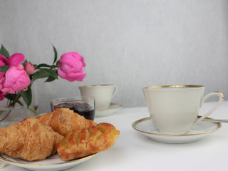 breakfast with two cups of coffee and croissants, bouquet of pink flowers