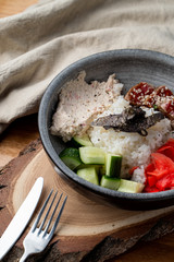 Eel poke bowl with rice, ginger and cucumber on wooden table with knife and fork
