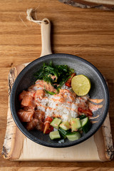 Raw salmon poke bowl with white rice, chuka and cucumber on wooden rustic table