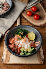 Raw salmon poke bowl with white rice, chuka and cucumber on wooden rustic table