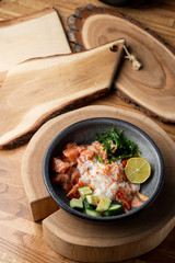 Raw salmon poke bowl with white rice, chuka and cucumber on wooden rustic table