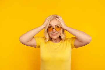 Exited pretty adult female in yellow T-shut and orange sunglasses with her hands on head
