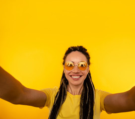 Cheerful woman in sunglasses making self photo in the yellow studio
