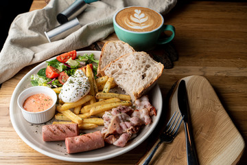 Substantial breakfast in a cafe with bacon, roasted sausage poached egg and salad