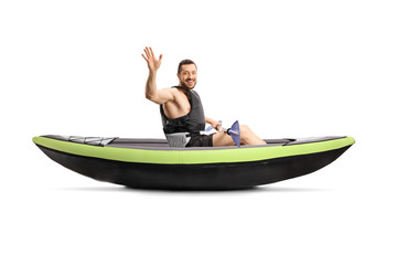 Young man with a paddle inside a kayak and waving at the camera