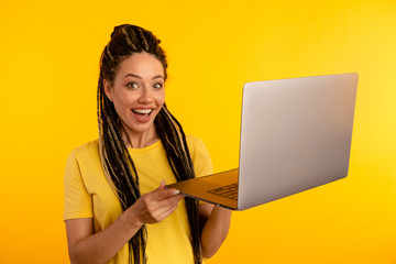 Portrait of happy exited young lady with laptop isolated over the yellow studio