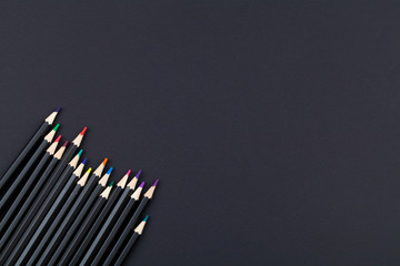 line of colored pencils on black background. top view close up flat lay copy space