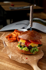Juicy beef burger with cheddar cheese and french fries on black background with selective focus