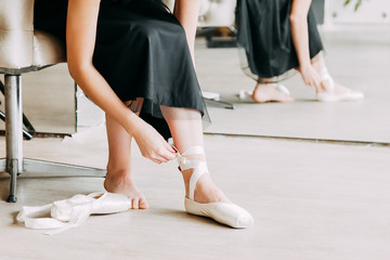 Feet of ballerina tying ribbons of her pointe shoes on light background. © Julia Kiseleva
