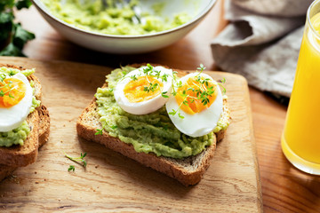Toast with avocado and boiled egg garnished with micro greens on a wooden table. Healthy breakfast food