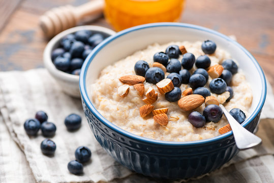 Oatmeal with blueberries and almonds in blue ceramic bowl on a wooden table. Closeup view of healthy breakfast food, vegan vegetarian meal