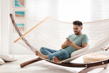 Young man using smartphone in hammock at home