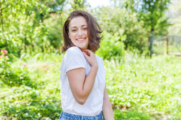 Fototapeta premium Happy girl smiling outdoor. Beautiful young brunete woman with brown hair resting on park or garden green background. European woman. Positive human emotion facial expression body language.