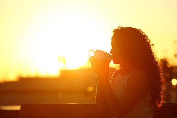 Silhouette of a woman drinking coffee at sunset