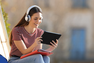 Happy student e learning with headphones and tablet in a campus