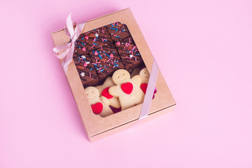 A set of sweets in a box with satin ribbon on the pink background. Shortbread cookies with heart, chocolate brownie.