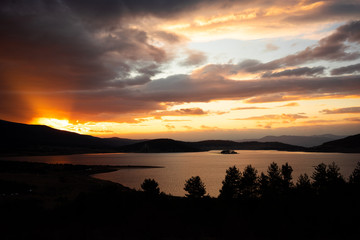 Obraz premium view of a lake during orange sunset framed by silhouettes of trees 