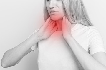 Female checking thyroid gland by herself. Close up of woman in white t- shirt touching neck with...