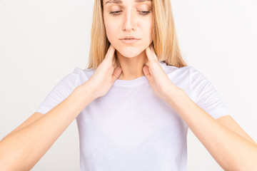 Female checking thyroid gland by herself. Close up of woman in white t- shirt touching neck with...