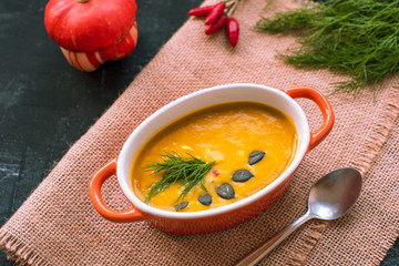 Pumpkin soup with ingredients: chili pepper and pumpkin seeds. Top view, black background.