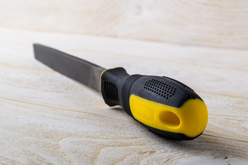 Flat steel file with black yellow rubber handle on a white wooden surface. Rasp tool for processing...