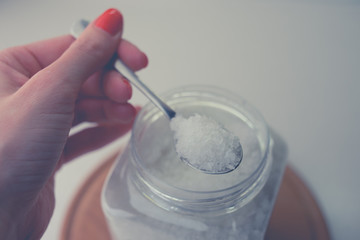 female hand holds a spoon with sea salt on the background of the container.