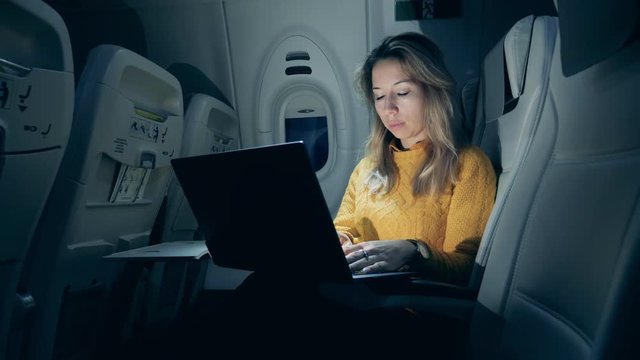 Aircraft cabin at night with a lady using a laptop