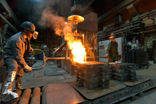 Workers In A Foundry Casting A Metal Workpiece - Safety At Work And Teamwork