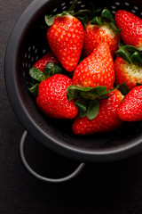 Fresh strawberries in a black colander on a black background, close up view