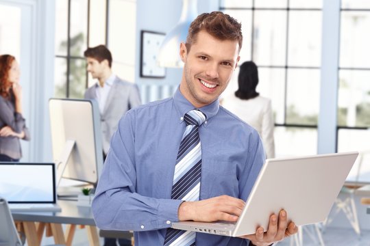 Happy young broker at business office with laptop