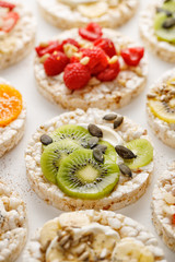 Rice wafers with a variety of fresh fruits, seeds, nuts and cream cheese on a white background, top view. Rice cakes, the concept of a healthy breakfast or dessert